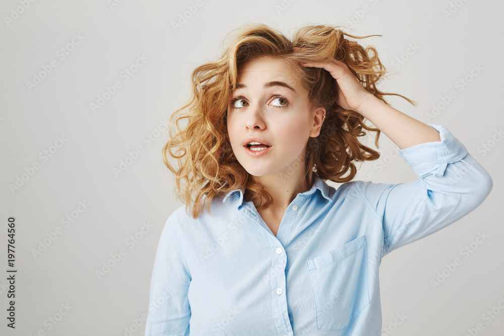 How do you like my new haircut. Portrait of cute trendy girl with short curly hair, checking hairstyle with hand and looking up, expressing misunderstanding or thinking over gray wall How do you like my new haircut. Portrait of cute trendy girl with short curly hair, checking hairstyle with hand and looking up, expressing misunderstanding or thinking over gray wall