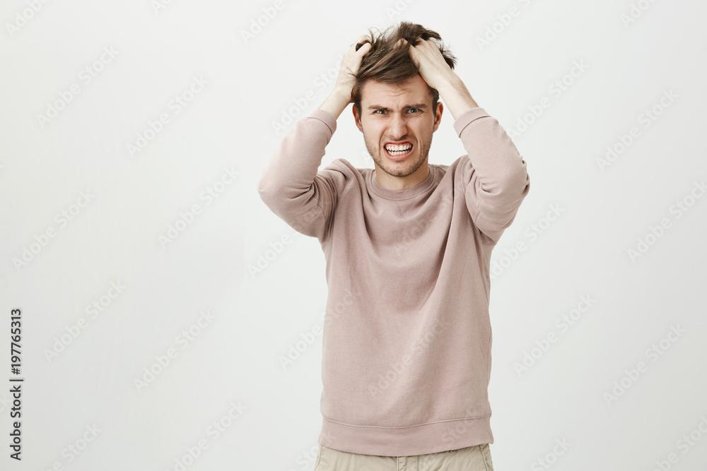 Portrait of very angry caucasian man pulling out his hair, being mad looking with furious expression at camera while standing against gray background. Boyfriend caught his fiancee cheating on him Portrait of very angry caucasian man pulling out his hair, being mad looking with furious expression at camera while standing against gray background. Boyfriend caught his fiancee cheating on him