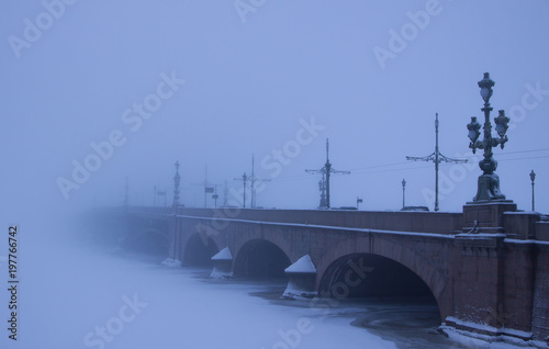 Scenic winter view of Trinity Bridge over  the frozen Neva River covered with snow in foggy morning. St.Petersburg, Russia.