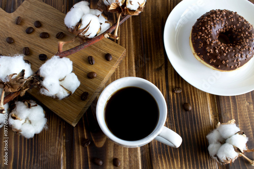 Composition with coffee branch of cottton and chocolate donut on the wooden background.Top view.