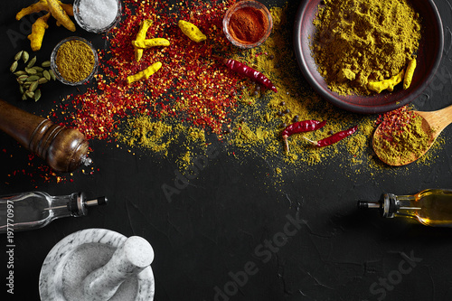 Cooking using fresh ground spices with mortar and small bowls of spice on a black table with powder spillage on its surface, overhead view with copyspace