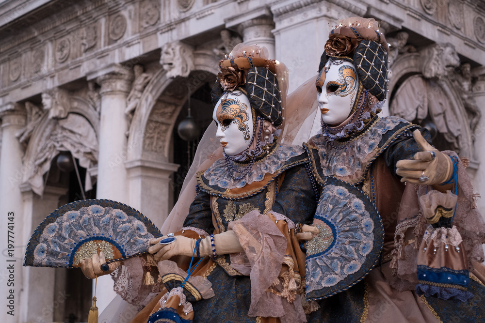 Obraz premium Two women in ornate costumes and painted masks, standing in St Marks Square during Venice Carnival (Carnivale di Venezia)