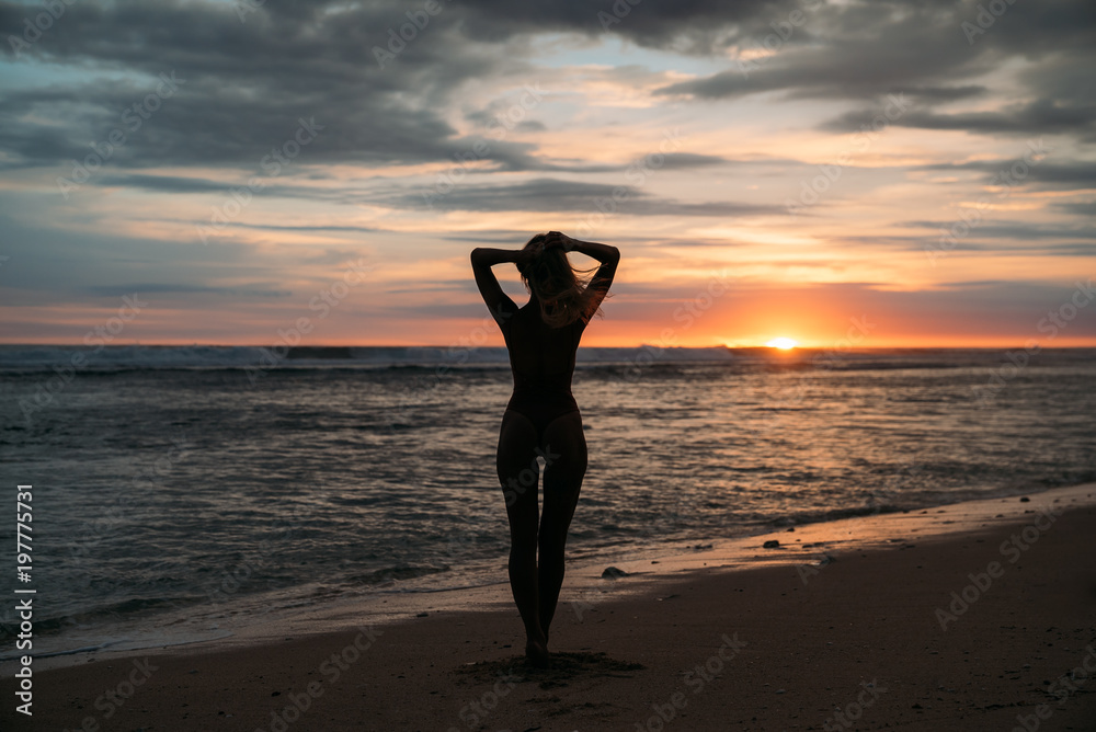 Back view silhouette of sexual woman. Beautiful young girl with long hair walking on the beach, posing at sunset. Concept of travel, relax, yoga