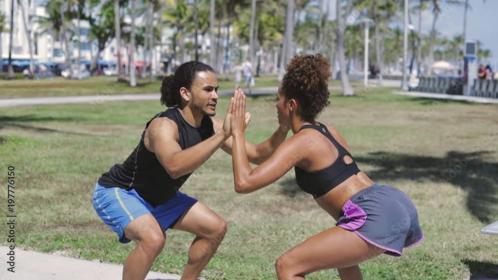 Side view of athletic ethnic man and woman knee bending and clapping hands while exercising in park in sunny day. Side view of athletic ethnic man and woman knee bending and clapping hands while exercising in park in sunny day.