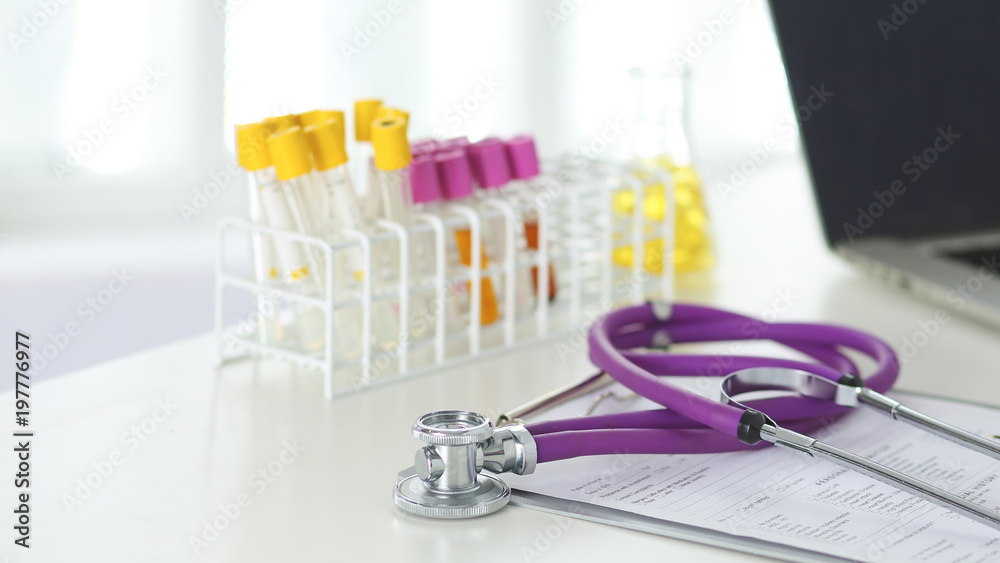 closeup of the desk of a doctors office with a stethoscope in the foreground and a bottle with pills in the background closeup of the desk of a doctors office with a stethoscope in the foreground and a bottle with pills in the background