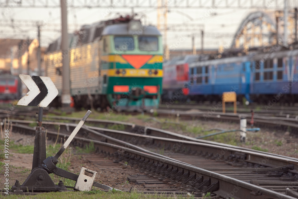Old manual hand operated railroad switch with old locomotives and railway depot on background at sunset, selective focus/ Transportation, railroad traffic management concept/ Arrow switching/ Old manual hand operated railroad switch with old locomotives and railway depot on background at sunset, selective focus/ Transportation, railroad traffic management concept/ Arrow switching/