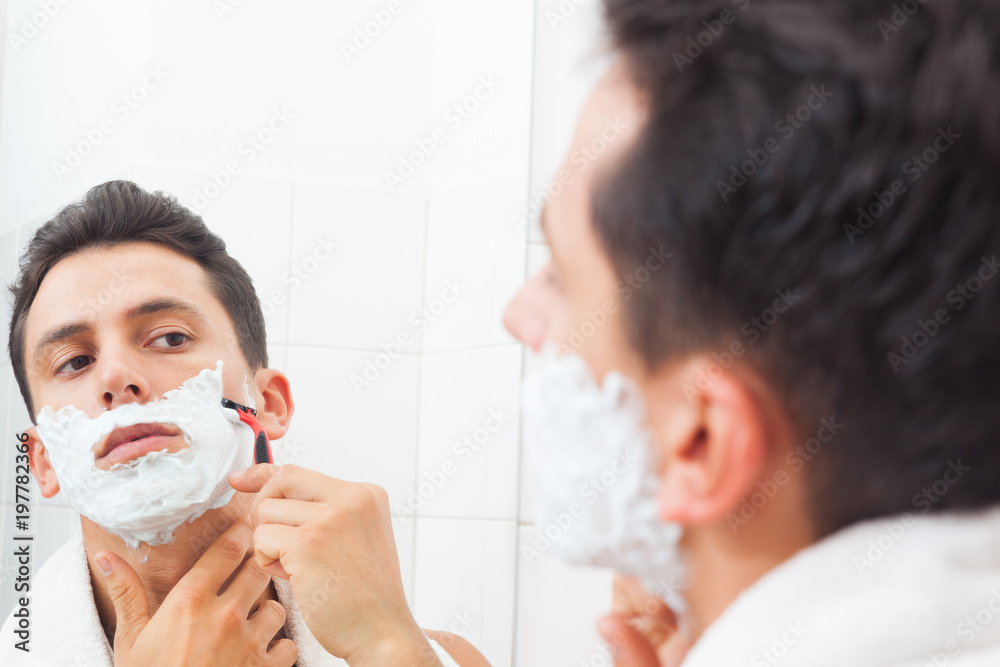Guy shaving his beard with razor at the bathroom