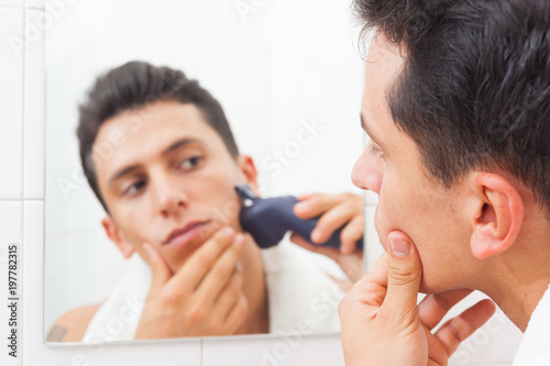 Young man in mirror shaving with electric shaver