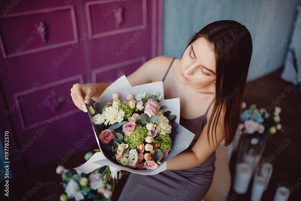 Naklejka premium Young woman holding bouquet of flowers in modern style of rose bush roses, feels scent of smell of spring.