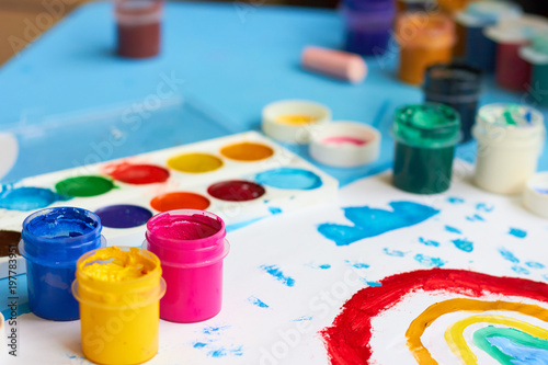  Paints, brushes and children's drawing on a blue table.