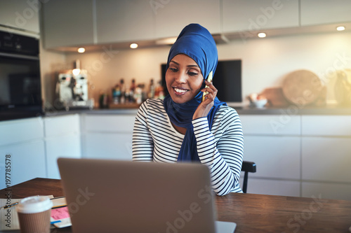 Smiling Arabic entrepreneur talking on a cellphone in her kitche