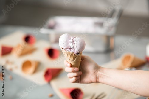 Holding waffle cone with ice cream at the kitchen with food ingredients on the background