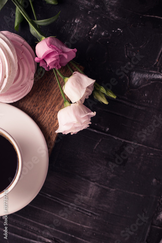 Coffee cup, lisianthus flower and raspberry meringue on dark desk. 