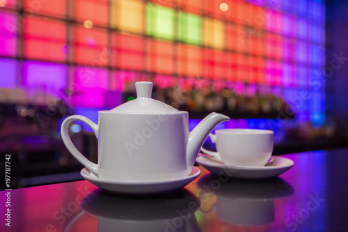 White teapot and tea cup on color lights background 