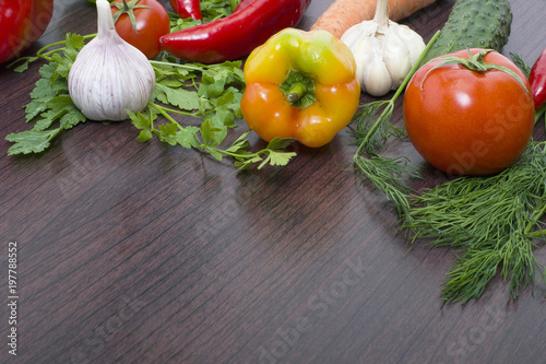 Red tomato and green cucumber. Red and yellow peppers with garlic on a wooden background.