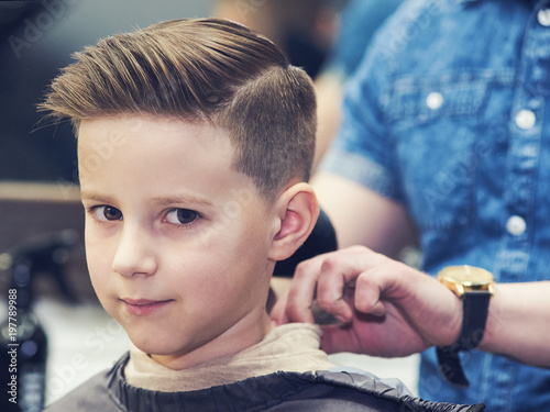 Barber shop. Boy with a totally new look is looking to a camera.