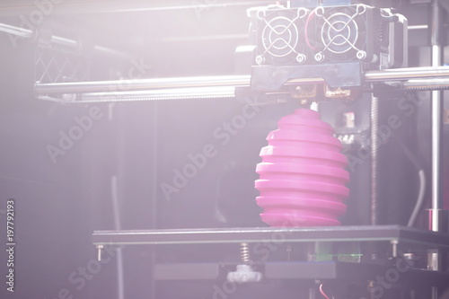 FDM 3D-printer manufacturing wound pink easter egg sculpture - diagonal view on print chamber object and print head - bright overshine light mood for background purpose - background blanked out blurry photo