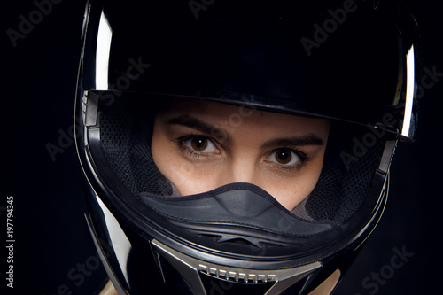 Confidence, sports and determination concept. Close up studio portrait of serious confident young woman motorcyclist with beautiful brown eyes wearing black protective helmet before motor race