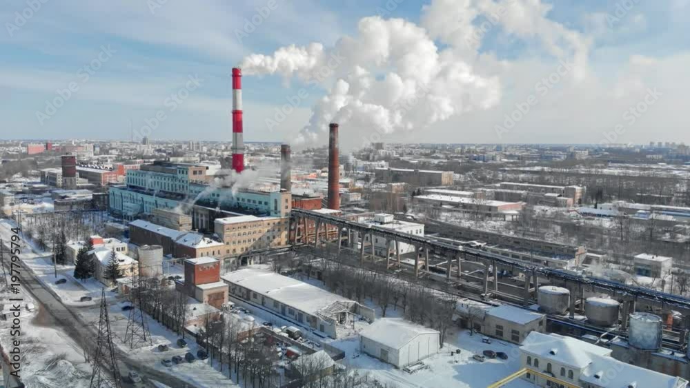 Dense thick smoke coming from industrial red-white pipes. Smooth aerial shooting of a power plant from a bird's eye view. Industrial environmental pollution with the fume.