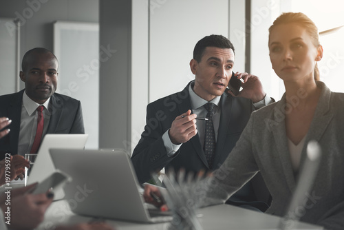 Young businessman distracting by a phone conversation while sitting at plenary session with coworkers