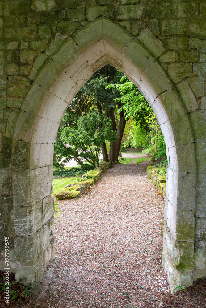 A Path Beyond the Arched Stone Wall in A European Abbey
