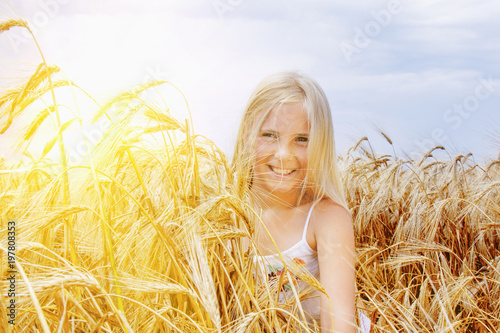 Happy young blonde girl against golden wheat field (summer rest, holiday, childhood concept)