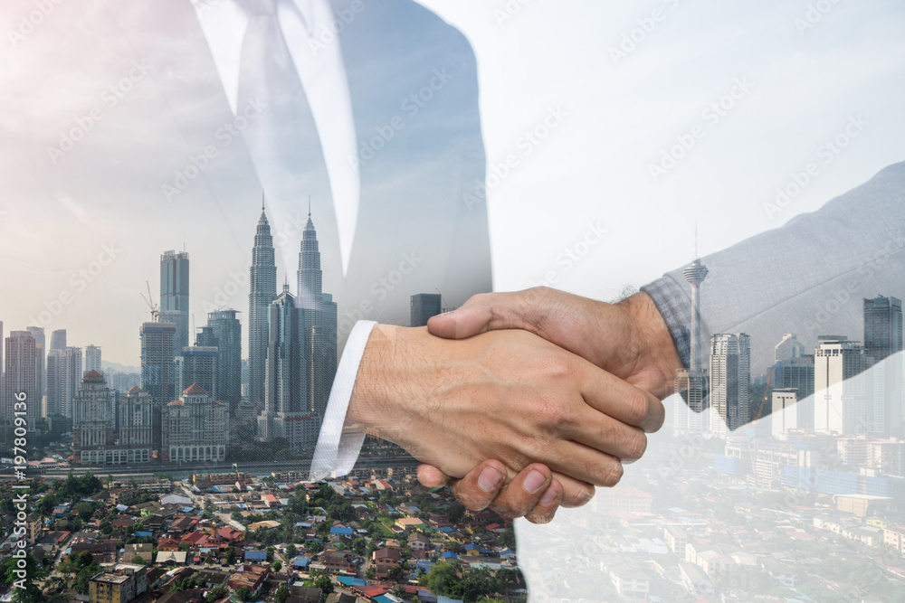 Naklejka premium Double Exposure of a businessman handshake on Kuala lumpur cityscape skyscraper Malaysia background.