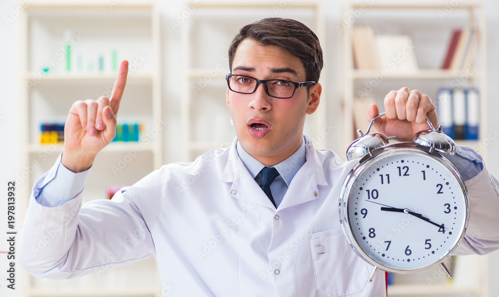 Young doctor with alarm clock in office clinic Young doctor with alarm clock in office clinic