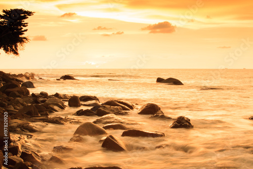 Gentle ocean waves on the rock beach at sunset.