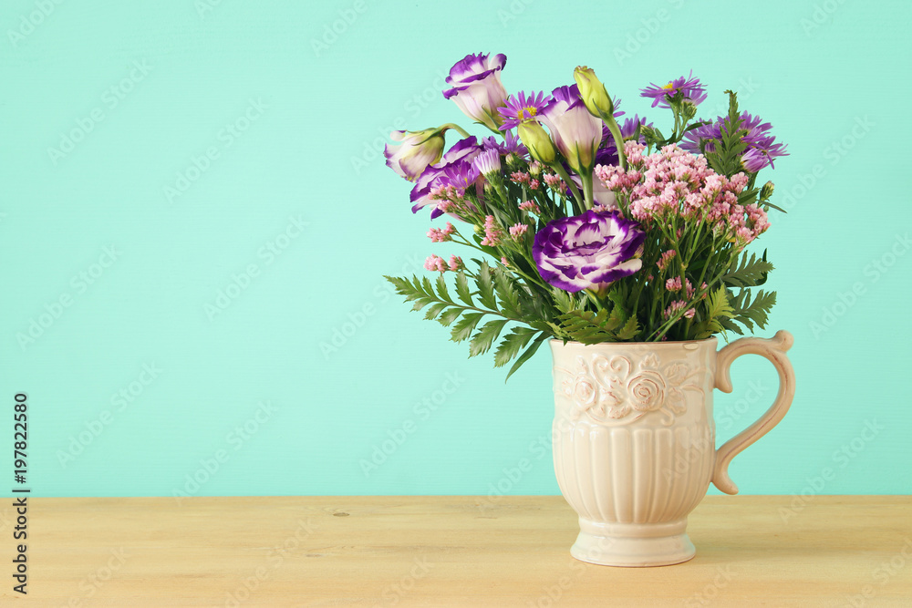 summer bouquet of purple flowers in the vase over wooden table and mint background.