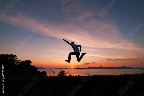 Asian man traveler is jumping on top of a rainforest mountain in scenery sunrise or sunset time background.