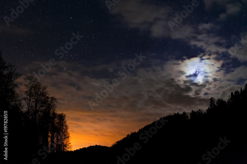 Night sky full of stars with waxing crescent of moon and sunset under them