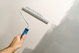 A man's hand with a paint roller against the backdrop of a painted ceiling. The concept of repair and painting the walls of the house.