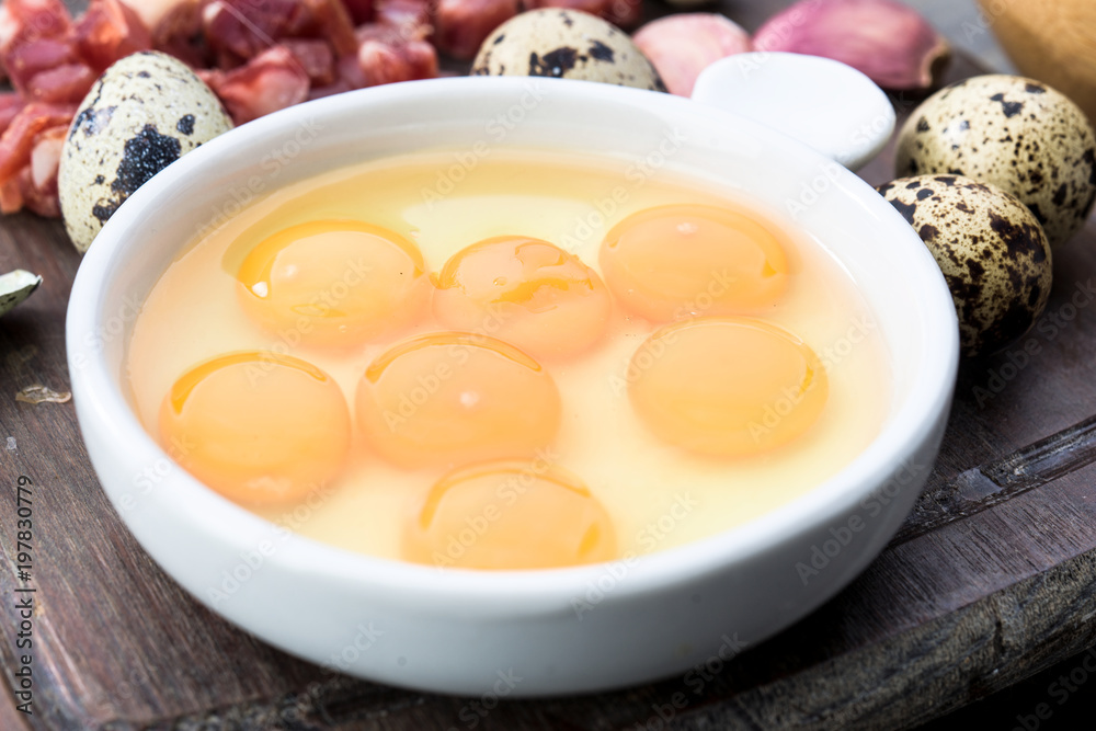 raw and open quail eggs in porcelain bowl, on rustic wood raw and open quail eggs in porcelain bowl, on rustic wood
