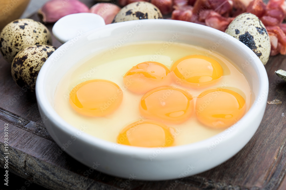 raw and open quail eggs in porcelain bowl, on rustic wood raw and open quail eggs in porcelain bowl, on rustic wood