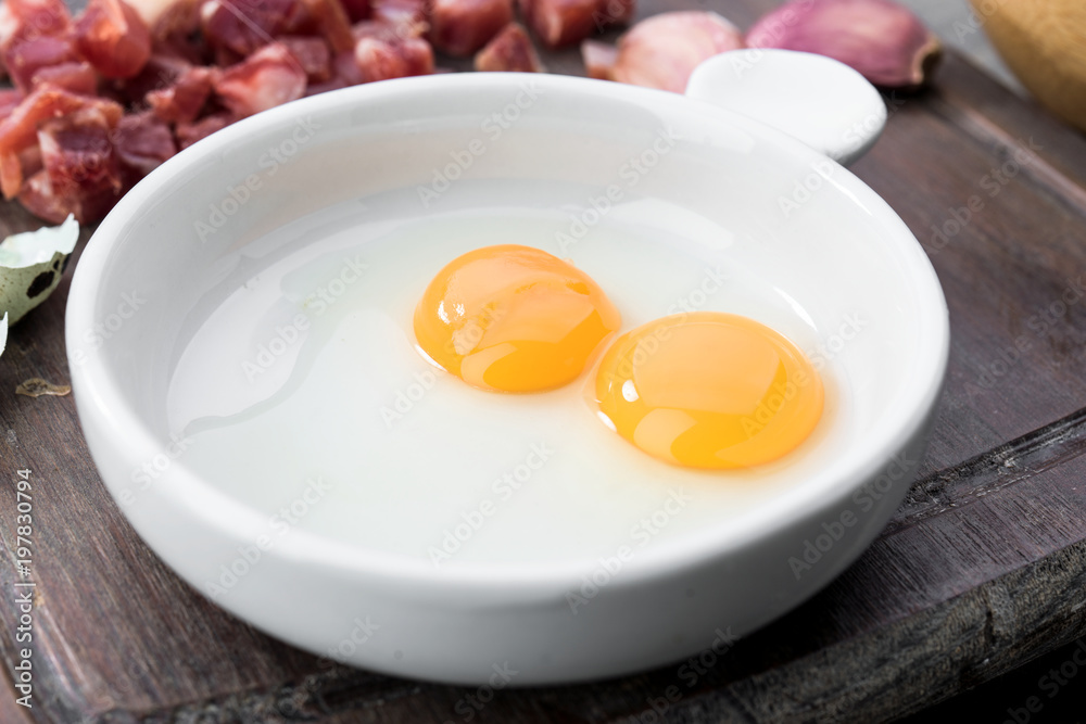 raw and open quail eggs in porcelain bowl, on rustic wood raw and open quail eggs in porcelain bowl, on rustic wood