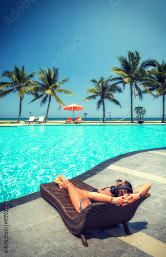 Woman at the swimming pool at the tropical resort with heaphones