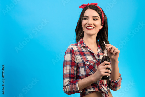 The happy girl standing with a bottle of drink on the blue background