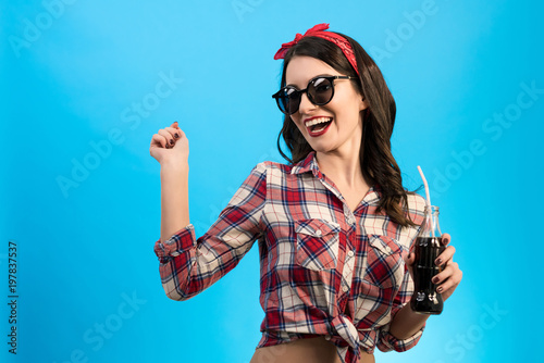 The girl in sunglasses standing with a bottle of drink on the blue background