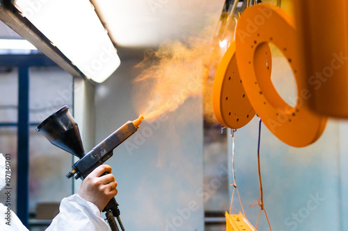 Powder coating of metal parts. A woman in a protective suit sprays powder paint from a gun on metal products photo
