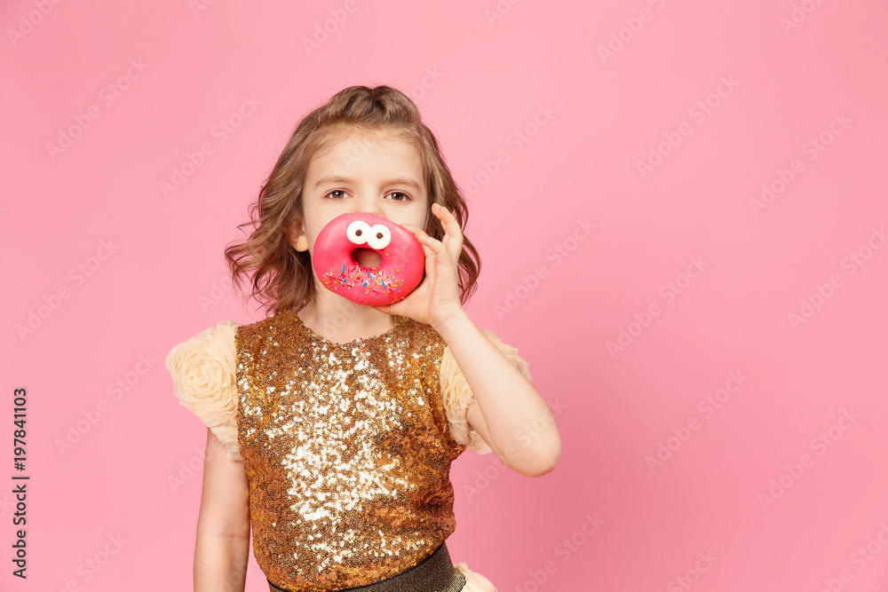 Surprised little girl in glittering dress standing with donuts posing on pink background. Surprised little girl in glittering dress standing with donuts posing on pink background.