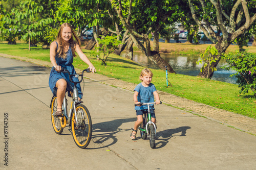 Happy family is riding bikes outdoors and smiling. Mom on a bike and son on a balancebike photo