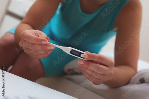 The concept of disease and ill health. Unidentified young woman in blue dress is holding thermometer