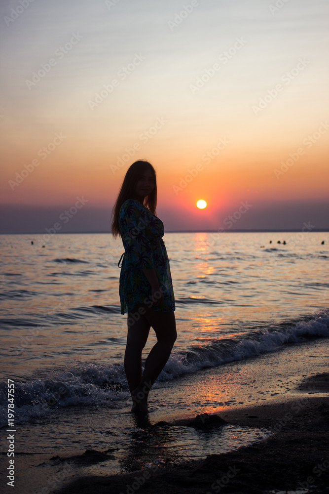 silhouette of a young, slender girl in the background of the setting sun on the beach, looking at the sunset