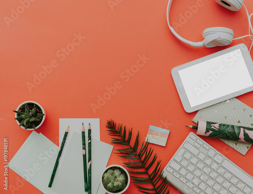 Flat lay trendy workspace with keyboard, diary, succulent and accessories on orange background. Top view