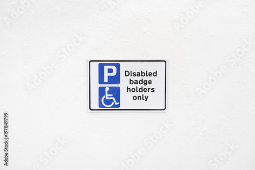 Disabled badge holders only sign on blank white wall at accessibly parking space at car park photo