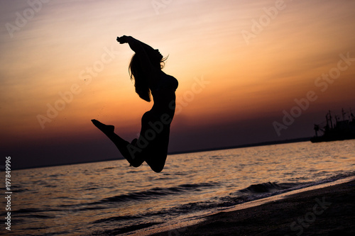 young  slender girl gracefully jumping on the sand in the sea at sunset. the concept of freedom of life. place under the text.