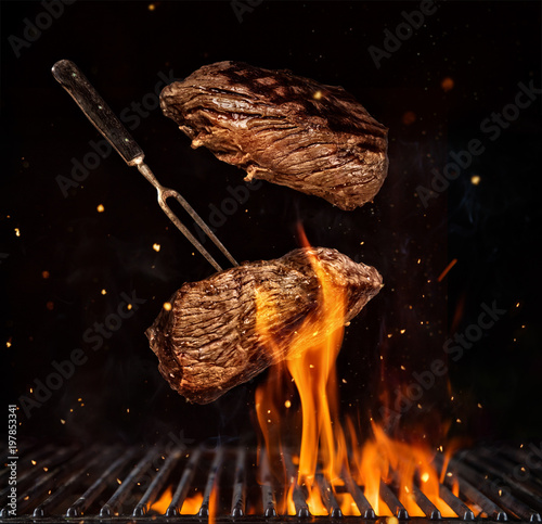 Fotografering Flying beef steaks over grill grid, isolated on black background