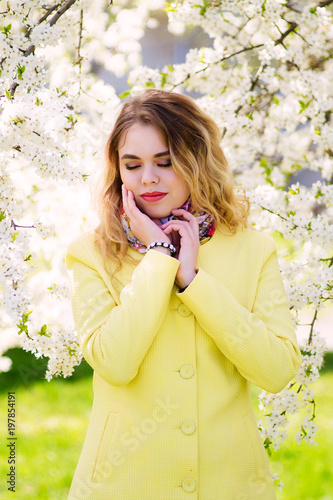 A young woman dressed in a fashionable yellow coat in a flowering park