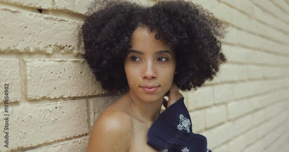 Headshot of young African-American girl with nude shoulders and short rich curls looking at camera leaning on wall.  Stock ビデオ | Adobe Stock 